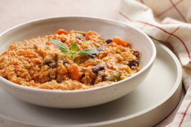 Tahıl tabağı - Millet domatesli, fasulyeli, havuçlu ve baharatlı, beton yuvarlak tepside beyaz bir kasede naneli, mor arka planda keten mutfak havlusu olan