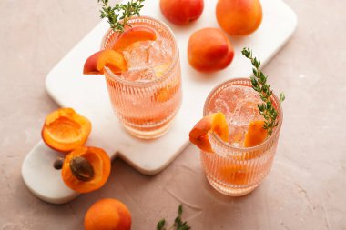 Buz küpleri, kayısı dilimleri ve soluk mor arka planda mermer tahtada taze kekik ile ferahlatıcı yaz kokteyli.