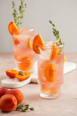 Buz küpleri, kayısı dilimleri ve soluk mor arka planda mermer tahtada taze kekik ile ferahlatıcı yaz kokteyli.