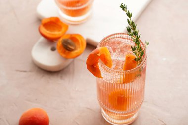 Buz küpleri, kayısı dilimleri ve soluk mor arka planda mermer tahtada taze kekik ile ferahlatıcı yaz kokteyli.