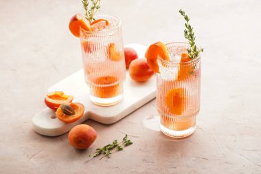 Buz küpleri, kayısı dilimleri ve soluk mor arka planda mermer tahtada taze kekik ile ferahlatıcı yaz kokteyli.