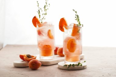 Buz küpleri, kayısı dilimleri ve soluk mor arka planda mermer tahtada taze kekik ile ferahlatıcı yaz kokteyli.