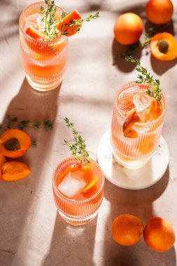 Buz küpleri, kayısı dilimleri ve soluk mor arka planda mermer tahtada taze kekik ile ferahlatıcı yaz kokteyli.