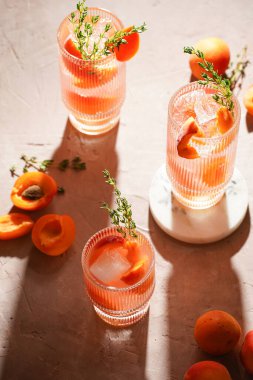 Buz küpleri, kayısı dilimleri ve soluk mor arka planda mermer tahtada taze kekik ile ferahlatıcı yaz kokteyli.