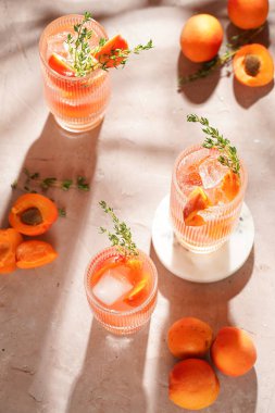 Buz küpleri, kayısı dilimleri ve soluk mor arka planda mermer tahtada taze kekik ile ferahlatıcı yaz kokteyli.