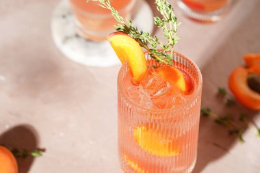 Buz küpleri, kayısı dilimleri ve soluk mor arka planda mermer tahtada taze kekik ile ferahlatıcı yaz kokteyli.