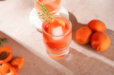 Buz küpleri, kayısı dilimleri ve soluk mor arka planda mermer tahtada taze kekik ile ferahlatıcı yaz kokteyli.