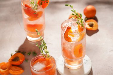 Buz küpleri, kayısı dilimleri ve soluk mor arka planda mermer tahtada taze kekik ile ferahlatıcı yaz kokteyli.