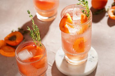 Buz küpleri, kayısı dilimleri ve soluk mor arka planda mermer tahtada taze kekik ile ferahlatıcı yaz kokteyli.