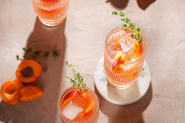 Buz küpleri, kayısı dilimleri ve soluk mor arka planda mermer tahtada taze kekik ile ferahlatıcı yaz kokteyli.