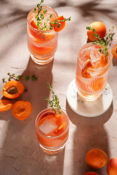 Buz küpleri, kayısı dilimleri ve soluk mor arka planda mermer tahtada taze kekik ile ferahlatıcı yaz kokteyli.