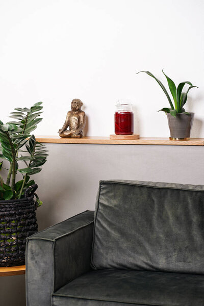 Decoration in interior: blank crimson pillar candle in glass jar without label on a wooden table in front of couch and indoor plant - a living room set-up