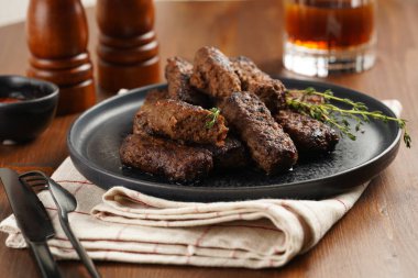 Geleneksel Güney Avrupa derisi yüzülmemiş sosisler, öğütülmüş et ve baharatlardan yapılmış mutfak havlusunda kekik ile birlikte siyah tabakta.