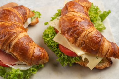 two lye croissant sandwiches with iberian ham, tomato slices, lettuce and cheese on marble board on grey background