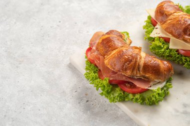 two lye croissant sandwiches with iberian ham, tomato slices, lettuce and cheese on marble board on grey background