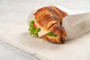 two lye croissant sandwiches with iberian ham, tomato slices, lettuce and cheese on marble board on grey background