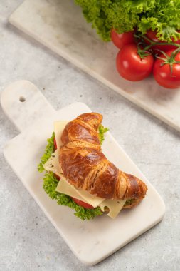 two lye croissant sandwiches with iberian ham, tomato slices, lettuce and cheese on marble board on grey background