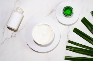 A mock-up of a round cosmetics container with cream on marble background and green palm leaf, top view
