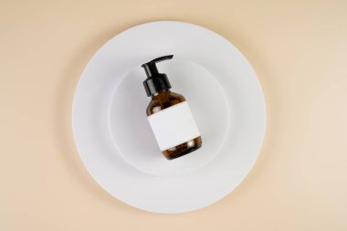 mock-up of brown cosmetics bottle with dispenser and white label on white round podium on beige colored background, top view