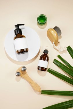A mock-up of a brown cosmetics bottle with dispenser and white label, bottle with pipette, face brush, face massage roller on beige colored background, top view