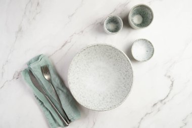 Empty grey ceramic scandy soup bowl, espresso coffee mugs and dip bowl, fork and knife on a marble surface and kitchen towel, top view