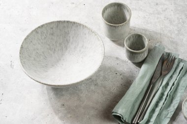 Empty grey ceramic scandy soup bowl, espresso coffee mugs and dip bowl, fork and knife on a marble surface and kitchen towel