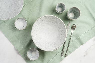 Empty grey ceramic scandy soup bowl, espresso coffee mugs and dip bowl, fork and knife on a marble surface and kitchen towel, top view