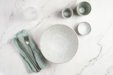 Empty grey ceramic scandy soup bowl, espresso coffee mugs and dip bowl, fork and knife on a marble surface and kitchen towel, top view