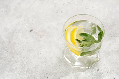 Morning beverage - a glass of lemon water with fresh mint on grey background, space for text
