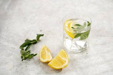 Morning beverage - a glass of lemon water with fresh mint on grey background, space for text