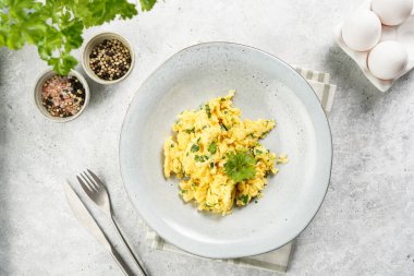 Kahvaltıda çırpılmış yumurta, yeşil otlar, gri masalarda maydanoz, antika çatal ve bıçak, üst manzara.