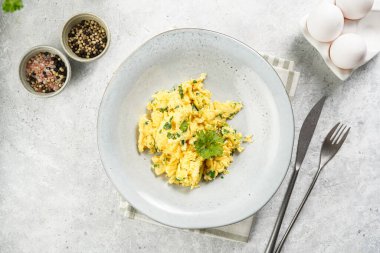 Kahvaltıda çırpılmış yumurta, yeşil otlar, gri masalarda maydanoz, antika çatal ve bıçak, üst manzara.