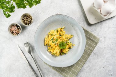 Kahvaltıda çırpılmış yumurta, yeşil otlar, gri masalarda maydanoz, antika çatal ve bıçak, üst manzara.