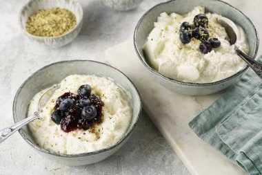 Sade beyaz İzlanda günlüğüyle iki gri kase reçelli gökyüzü, taze yaban mersini, gri arka planda kenevir tohumu