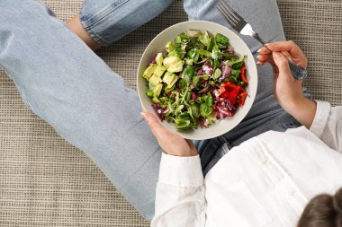 Kot pantolon giyen ve beyaz gömlekli bir kadın salatalı gri bir kâse ve yemeye hazır bir çatal tutuyor, sağlıklı yaşam tarzı konsepti.