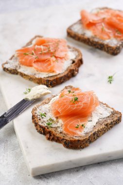 Krem peynirli kepekli ekmek sandviçi ve misket tahtasında limon dilimleri ve ekşi kremayla füme somon.
