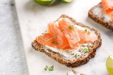 Krem peynirli kepekli ekmek sandviçi ve misket tahtasında limon dilimleri ve ekşi kremayla füme somon.