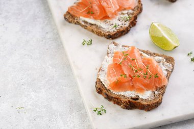 Krem peynirli kepekli ekmek sandviçi ve misket tahtasında limon dilimleri ve ekşi kremayla füme somon.