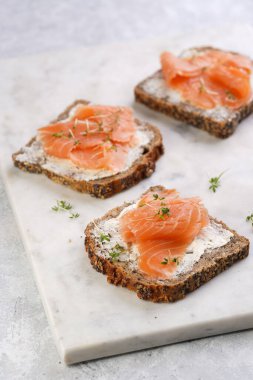 Krem peynirli kepekli ekmek sandviçi ve misket tahtasında limon dilimleri ve ekşi kremayla füme somon.