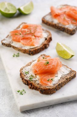 Krem peynirli kepekli ekmek sandviçi ve misket tahtasında limon dilimleri ve ekşi kremayla füme somon.