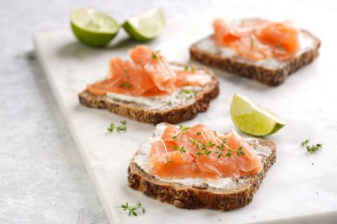 Krem peynirli kepekli ekmek sandviçi ve misket tahtasında limon dilimleri ve ekşi kremayla füme somon.
