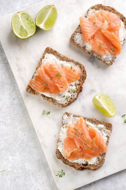 Krem peynirli kepekli ekmek sandviçi ve misket tahtasında limon dilimleri ve ekşi kremayla füme somon.