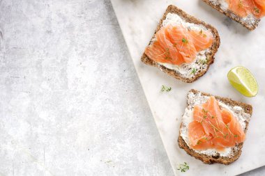 Krem peynirli tam buğday ekmekli sandviç ve misket tahtasında limon dilimleri ve ekşi kremayla füme somon. Üst görünüm, metin için boşluk