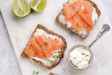 Krem peynirli kepekli ekmek sandviçi ve misket tahtasında limon dilimleri ve ekşi kremayla füme somon.