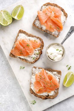 Krem peynirli kepekli ekmek sandviçi ve misket tahtasında limon dilimleri ve ekşi kremayla füme somon.