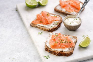 Krem peynirli kepekli ekmek sandviçi ve misket tahtasında limon dilimleri ve ekşi kremayla füme somon.