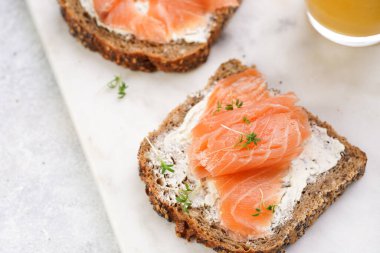 Krem peynirli kepekli ekmek sandviçi ve misket tahtasında limon dilimleri ve ekşi kremayla füme somon.