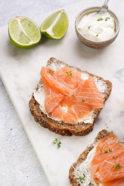 Krem peynirli kepekli ekmek sandviçi ve misket tahtasında limon dilimleri ve ekşi kremayla füme somon.