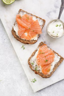 Krem peynirli kepekli sandviç ve misket tahtasında füme somon, limon dilimleri ve ekşi krema.