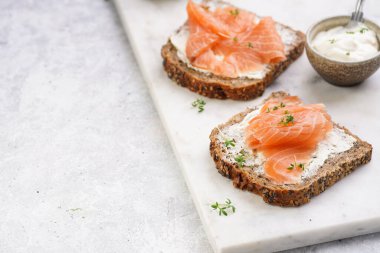 Krem peynirli kepekli ekmek sandviçi ve misket tahtasında limon dilimleri ve ekşi kremayla füme somon.